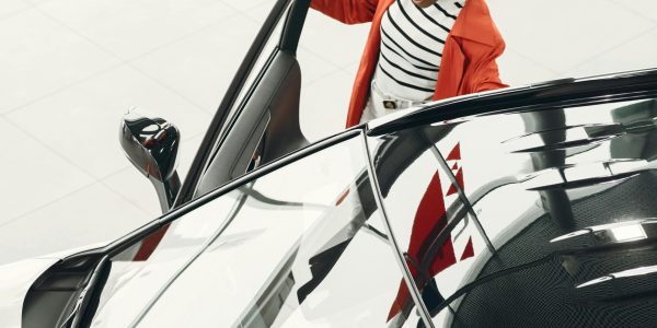 High angle view of woman inspecting sleek black car indoors. Stylish auto showroom.