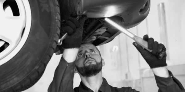 A mechanic inspects a car's underbody in a workshop, showcasing repair skills.